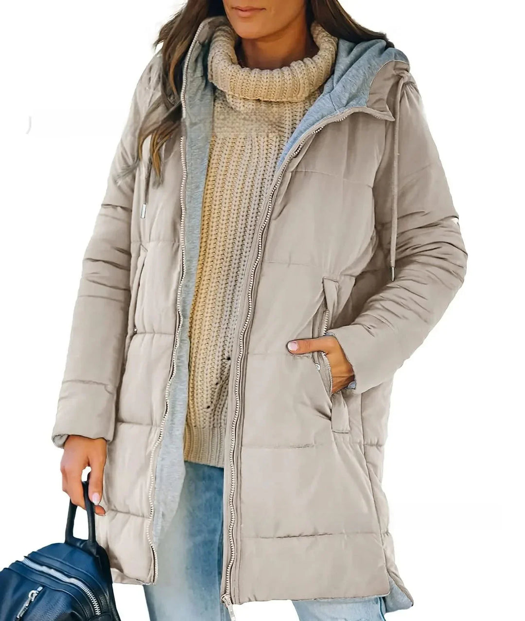 Woman wearing beige padded winter coat with gray hoodie, beige knit sweater, light blue jeans, holding black bag