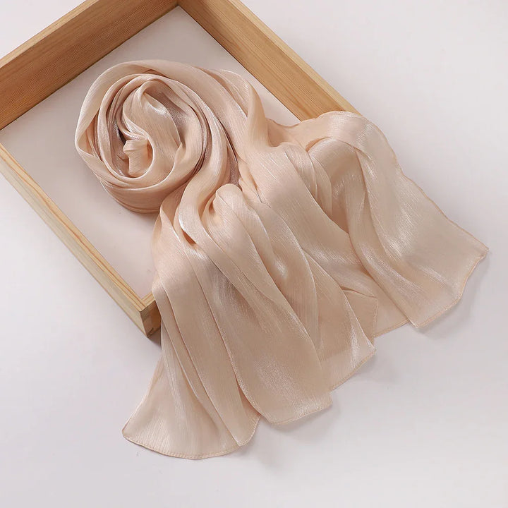 Light beige silky chiffon scarf partially rolled on wooden tray against white background