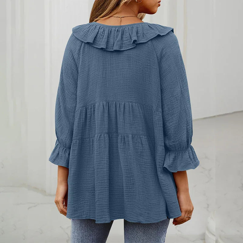 Back view of woman wearing textured blue ruffled collar blouse with 3/4 sleeves in bright indoor setting