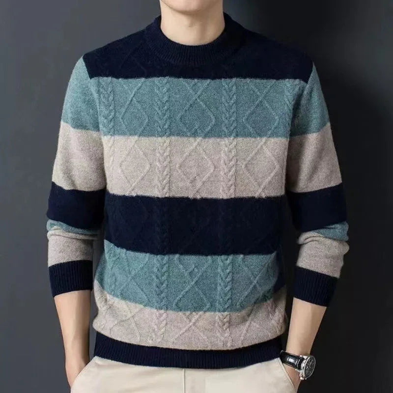 Man wearing striped blue, gray, and beige cable knit sweater with beige pants against dark background