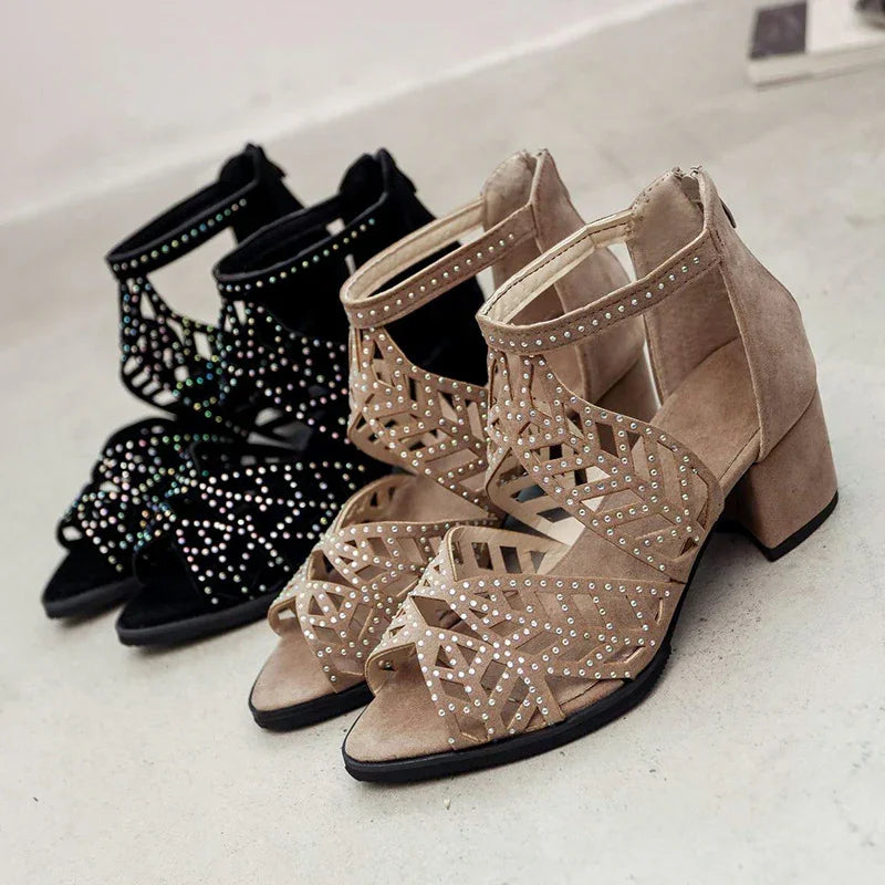 Pair of beige and black studded high heel sandals with geometric cutout design on concrete floor