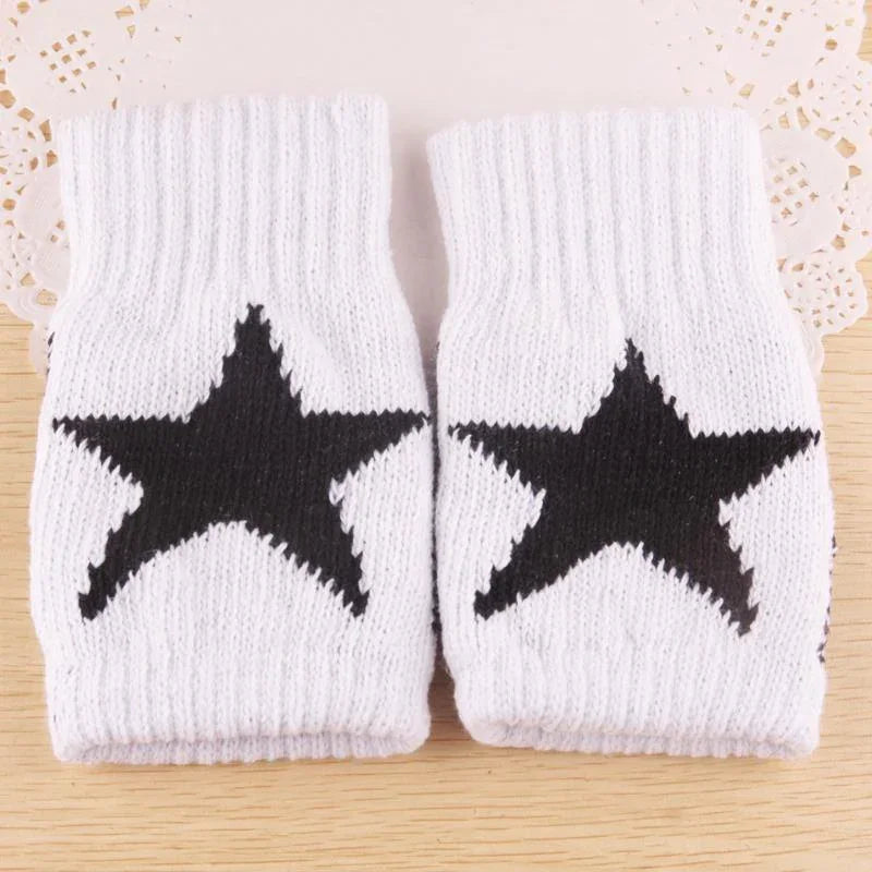 Pair of white knit wrist warmers with black star patterns on wooden surface