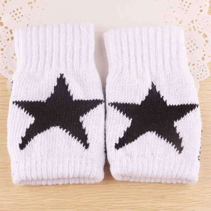 Pair of white knit wrist warmers with black star patterns on wooden surface
