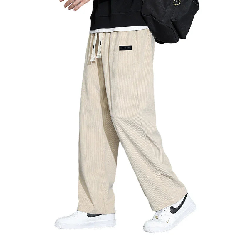 Person wearing beige wide-leg corduroy pants with drawstring and white Nike sneakers on white background