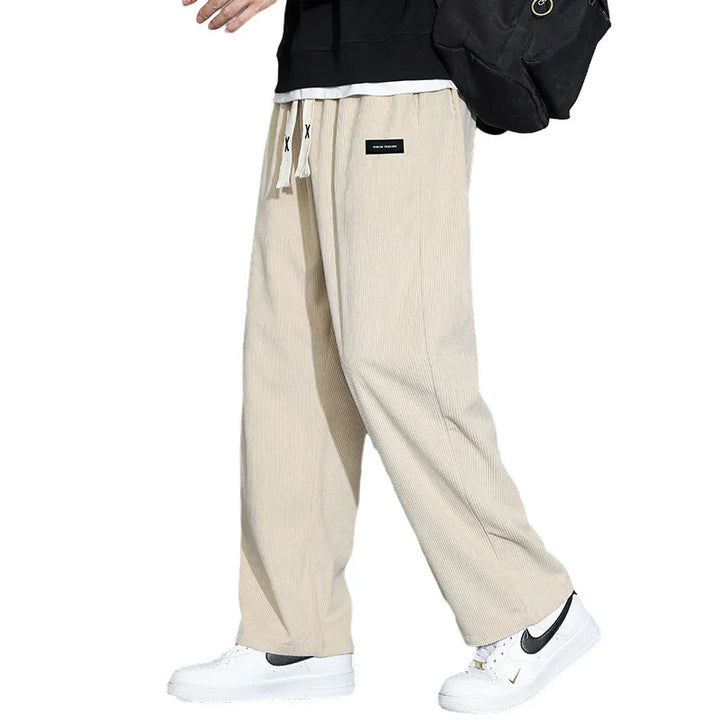 Person wearing beige wide-leg corduroy pants with drawstring and white Nike sneakers on white background