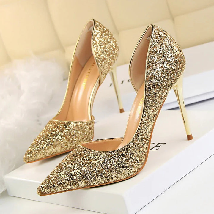Sparkling gold glitter high heel shoes with pointed toes on a white surface