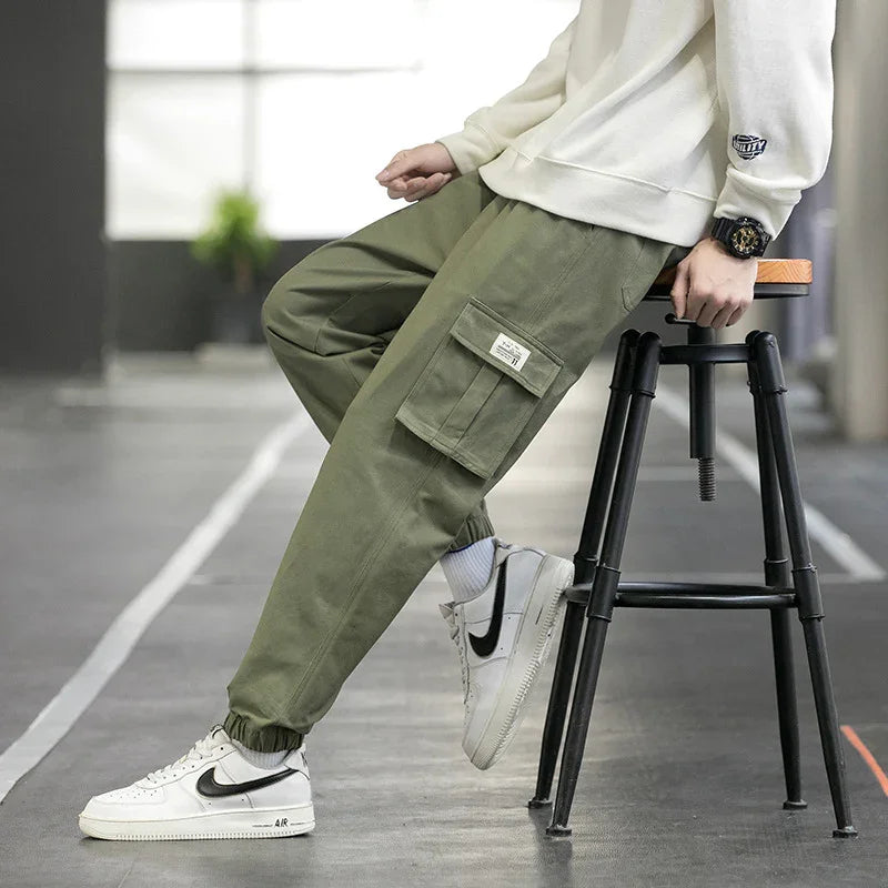 Person wearing olive green cargo pants with elastic cuffs and white Nike Air sneakers sitting on a black stool indoors