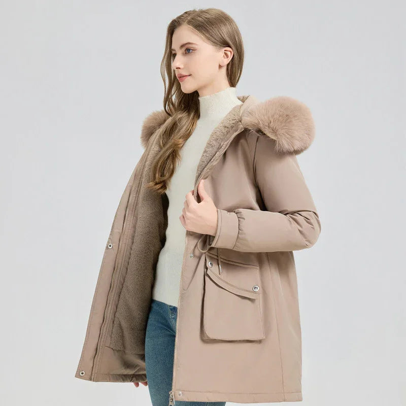 Woman wearing beige winter jacket with fur hood and cozy inner lining, paired with white turtleneck and jeans