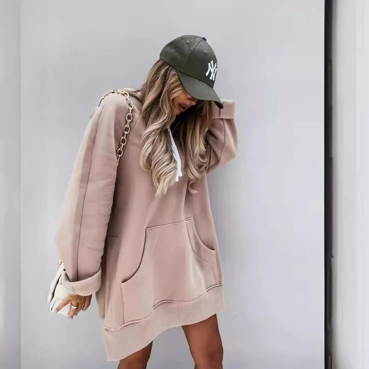 Woman wearing beige oversized hoodie dress and dark green New York baseball cap with long wavy hair