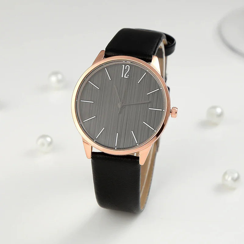Rose gold wristwatch with black leather strap and gray minimalist dial on white background with pearls