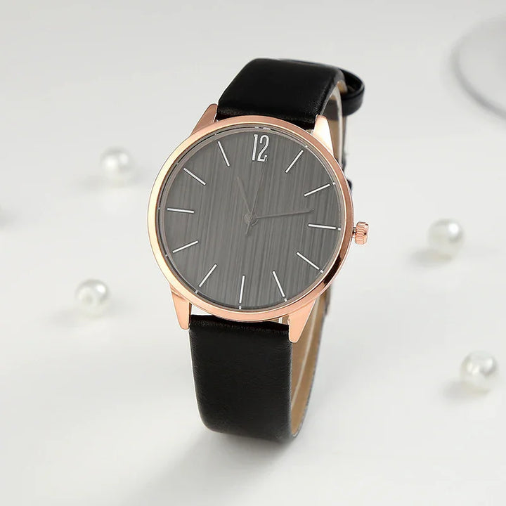 Rose gold wristwatch with black leather strap and gray minimalist dial on white background with pearls