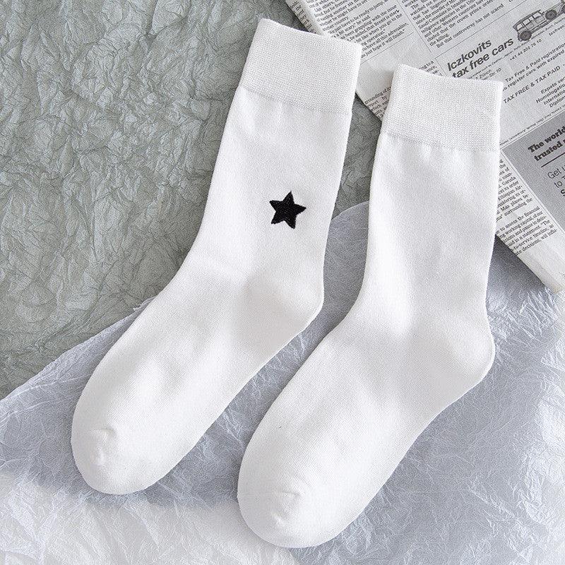 Pair of white crew socks with a single black star on one sock, placed on textured gray and white fabric with newspaper background