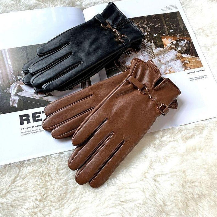 Black and brown leather gloves with buckle details placed on an open magazine on a soft white surface
