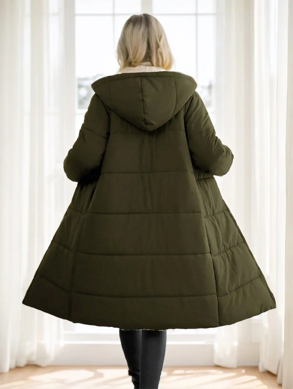 Woman wearing a long olive green quilted hooded winter coat indoors by a window