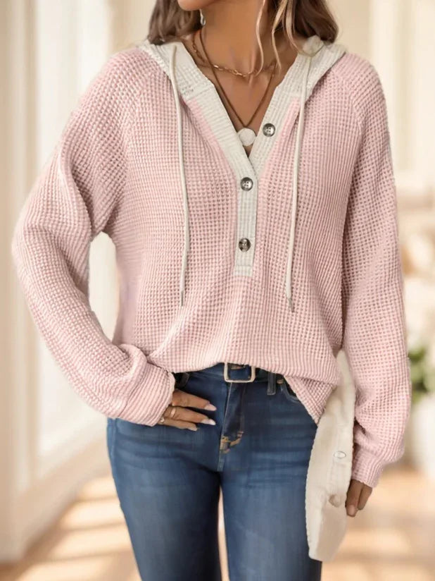 Woman wearing a pink waffle knit hoodie with buttons and blue jeans, casual indoor setting