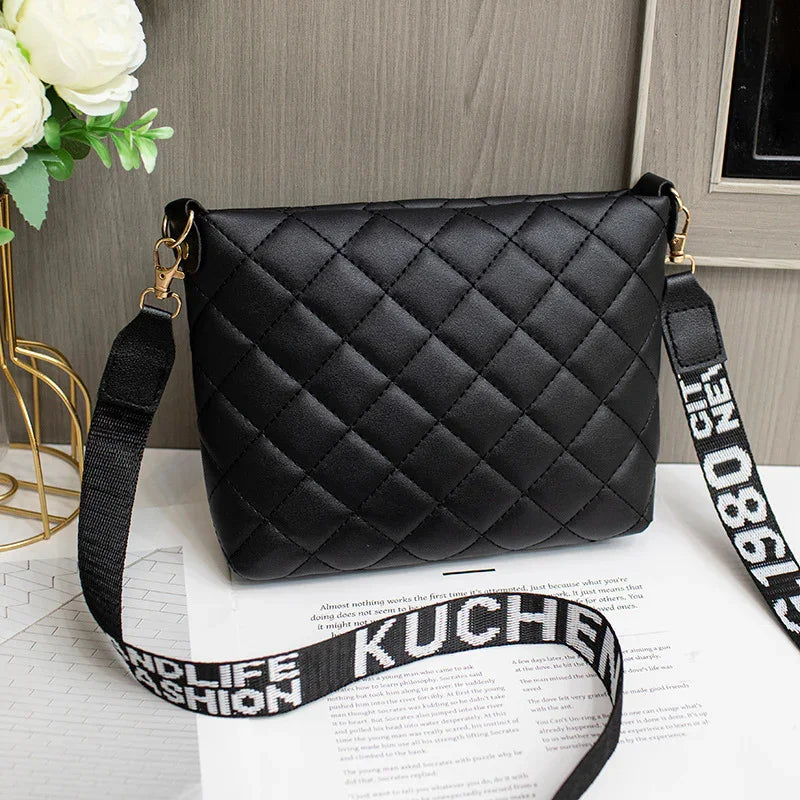Black quilted crossbody bag with wide adjustable strap featuring white text design
