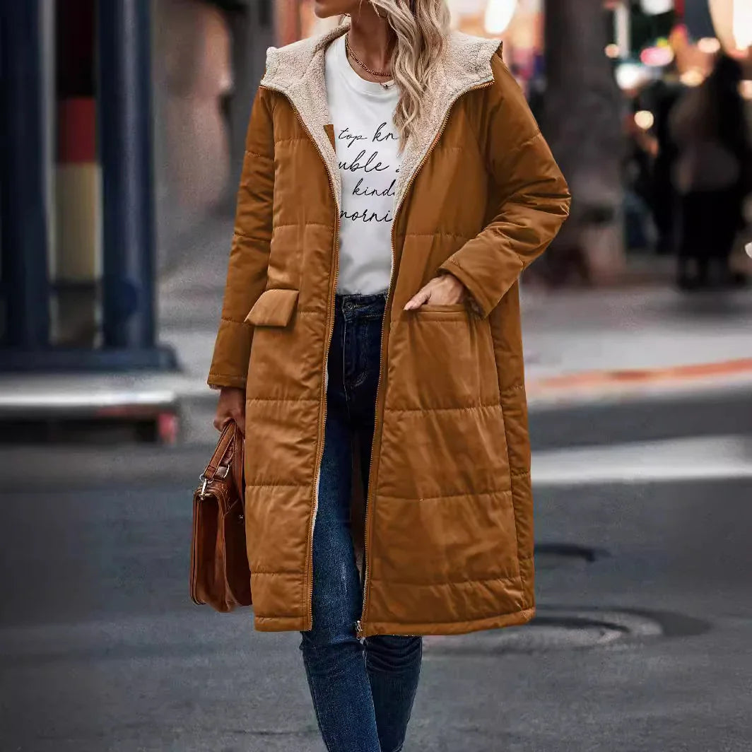Woman wearing long brown puffer coat with sherpa-lined hood, blue jeans, and carrying brown handbag on city street