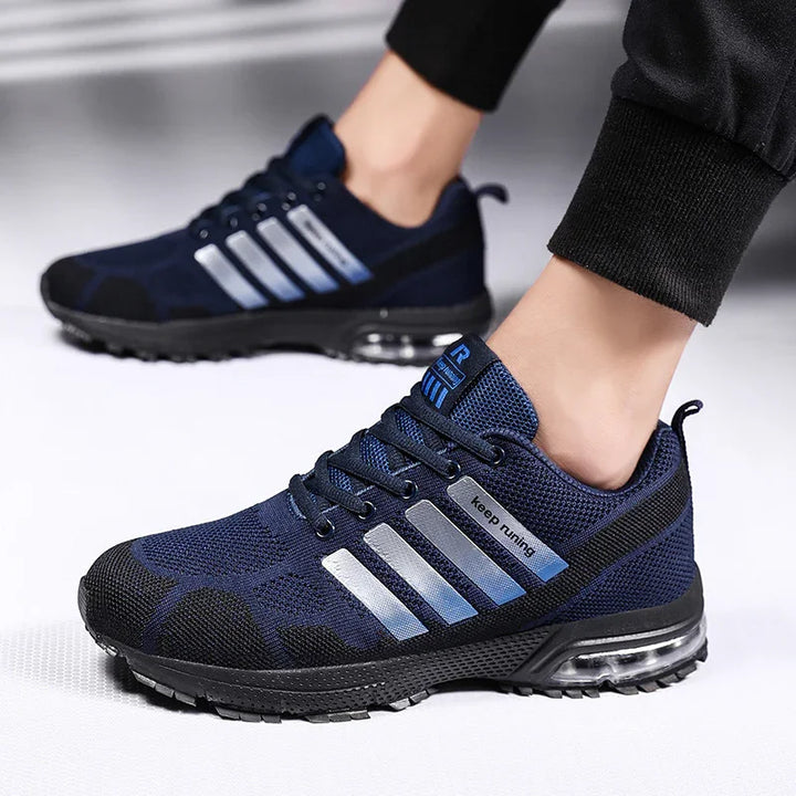 Navy blue running shoes with silver stripes and 'keep running' tag worn with black joggers