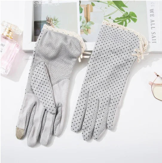 Pair of elegant grey women's gloves with black polka dots and lace trim, styled with perfume and sunglasses