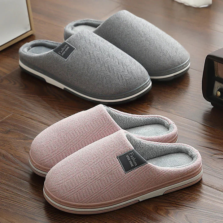 Pair of cozy indoor slippers in pink and gray with herringbone pattern on wooden floor