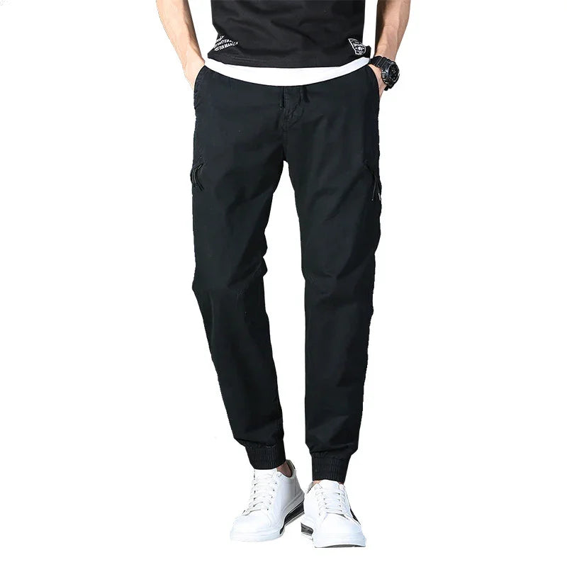 Men's black jogger pants with elastic cuffs paired with white sneakers and black t-shirt