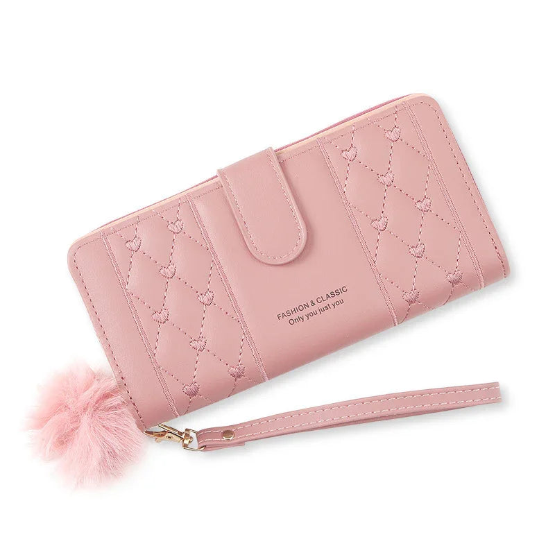 Pink quilted wallet with heart stitching, wrist strap, and fluffy pom-pom accessory, fashion classic design