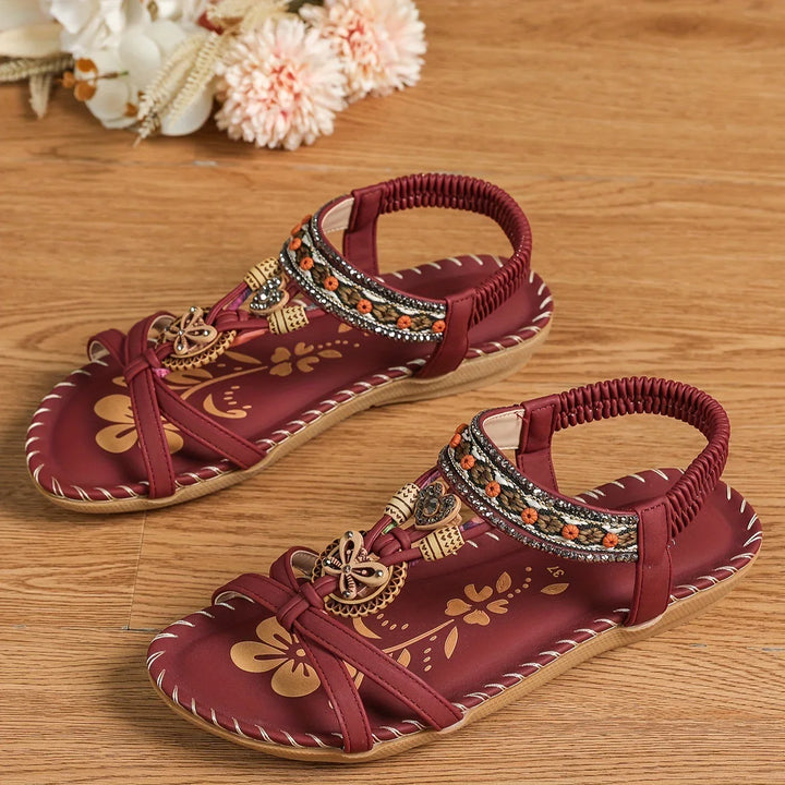 Maroon women's sandals with floral patterns and decorative beads on wooden floor