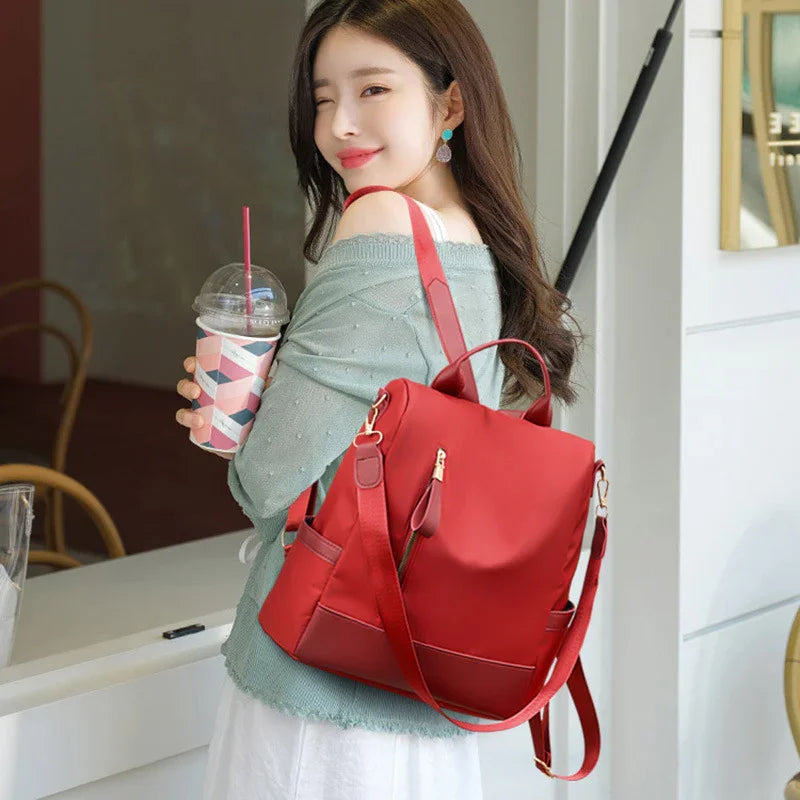 Young woman wearing light blue sweater and white skirt, carrying red backpack and holding a drink