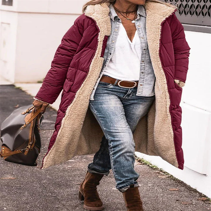 woman wearing long burgundy puffer coat with beige fleece lining, blue jeans, white top, brown boots, carrying brown handbag