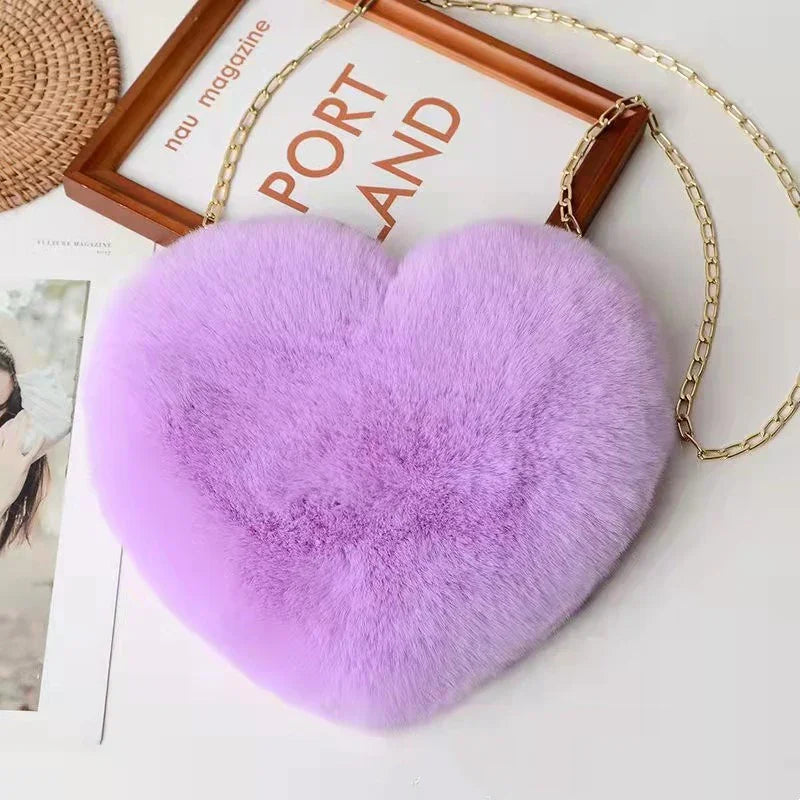 Soft fluffy lavender heart-shaped purse with gold chain strap on magazine background