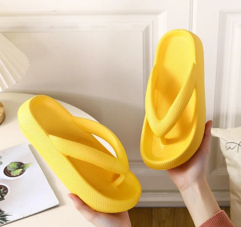 Bright yellow foam platform flip flops held in hands against white paneled wall background