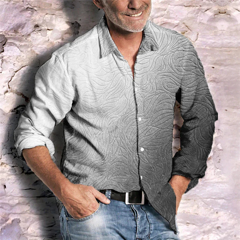 Smiling man in casual shirt with textured pattern and rolled-up sleeves, standing against rustic brick wall