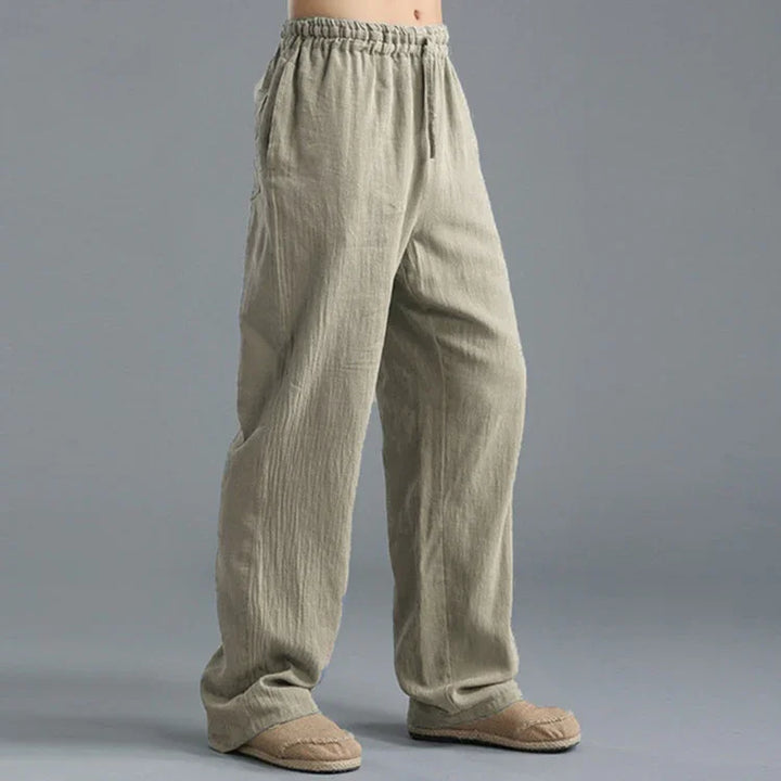 Person wearing loose beige linen pants with elastic waistband and slip-on shoes on gray background