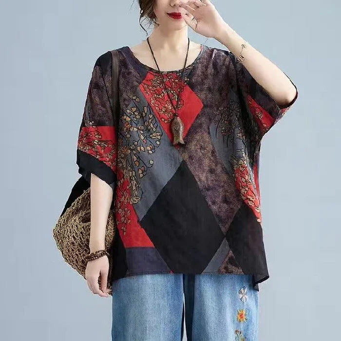 Woman wearing loose, patterned top with red, black and gray geometric design and blue jeans with floral embroidery