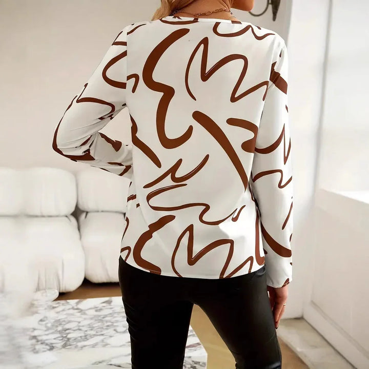Woman wearing white long-sleeve blouse with abstract brown pattern, standing in modern living room
