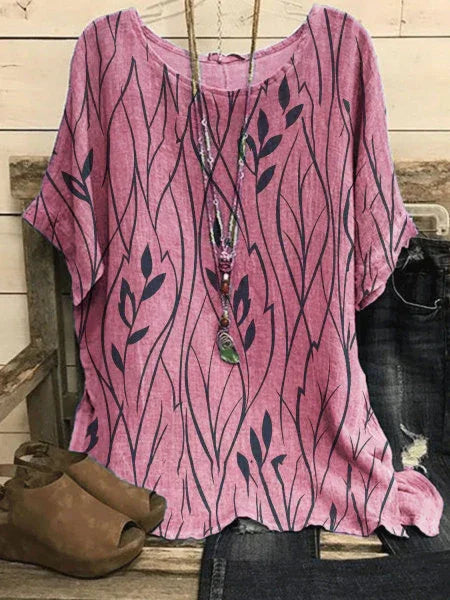 Pink short-sleeve blouse with black leaf and vine pattern, paired with distressed jeans and brown open-toe ankle boots