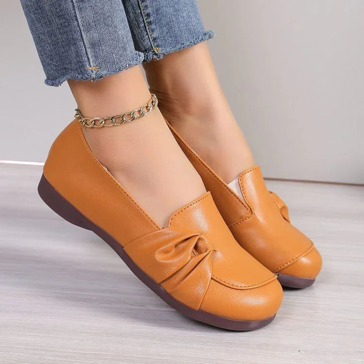 Women's tan leather slip-on flats with gathered detail, worn with cropped denim jeans and gold chain anklet
