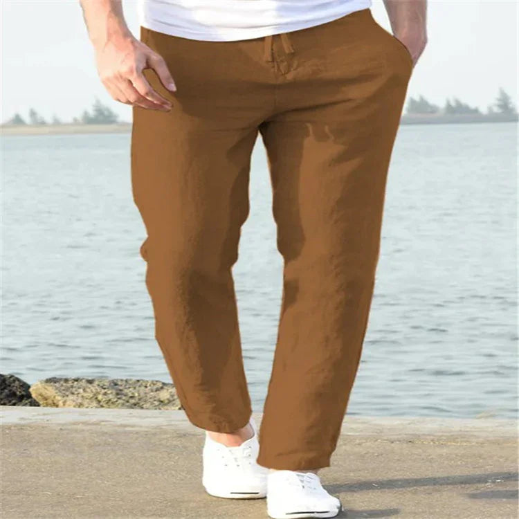 Man wearing brown casual pants and white sneakers walking by the waterfront on a sunny day