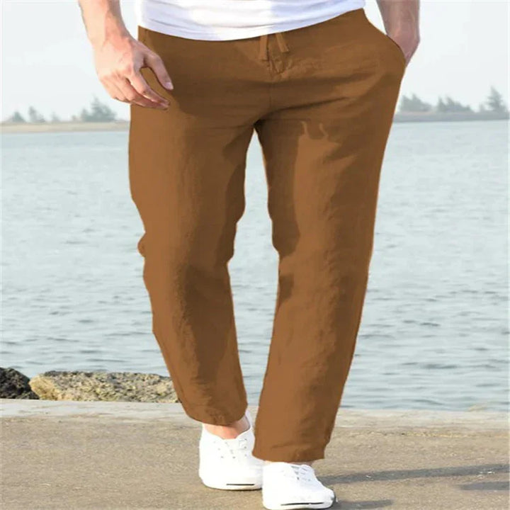 Man wearing brown casual pants and white sneakers walking by the waterfront on a sunny day