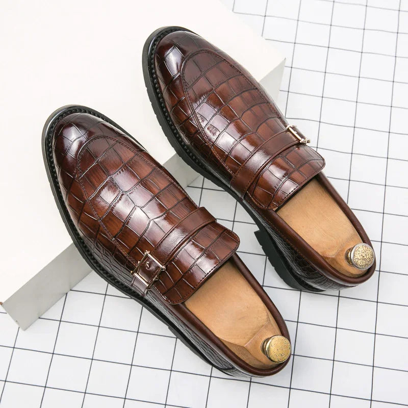Pair of men's brown crocodile pattern leather loafers with wooden shoe trees on checkered floor