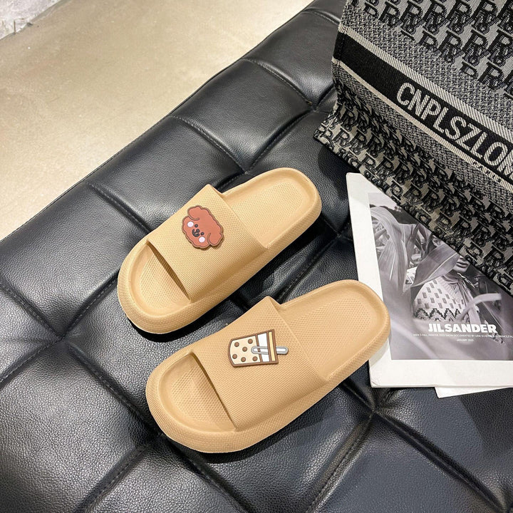 Beige slide sandals with cartoon dog and bubble tea charms on black leather surface, next to patterned bag and Jil Sander magazine