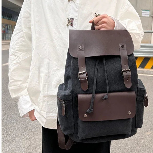 Person in white shirt holding black backpack with brown leather straps and front pocket on street