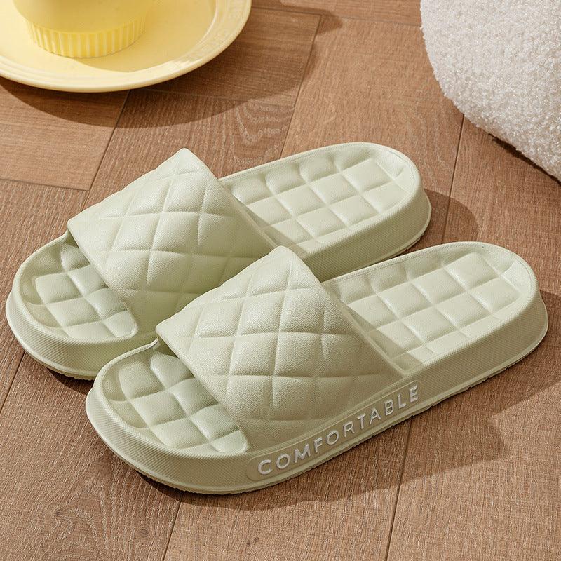 Pair of light green quilted indoor slippers with cushioned soles labeled comfortable on wooden floor