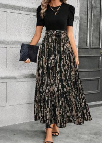 woman wearing black puff sleeve top with patterned long flowy skirt and holding black clutch in modern hallway