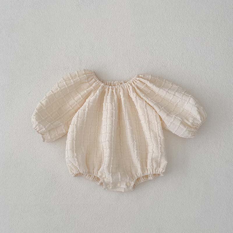 Cream textured baby romper with puffed long sleeves and snap closures on beige background