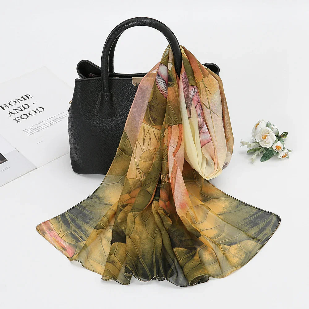 Black leather handbag with floral patterned silk scarf draped over it, white flowers and magazine on white background