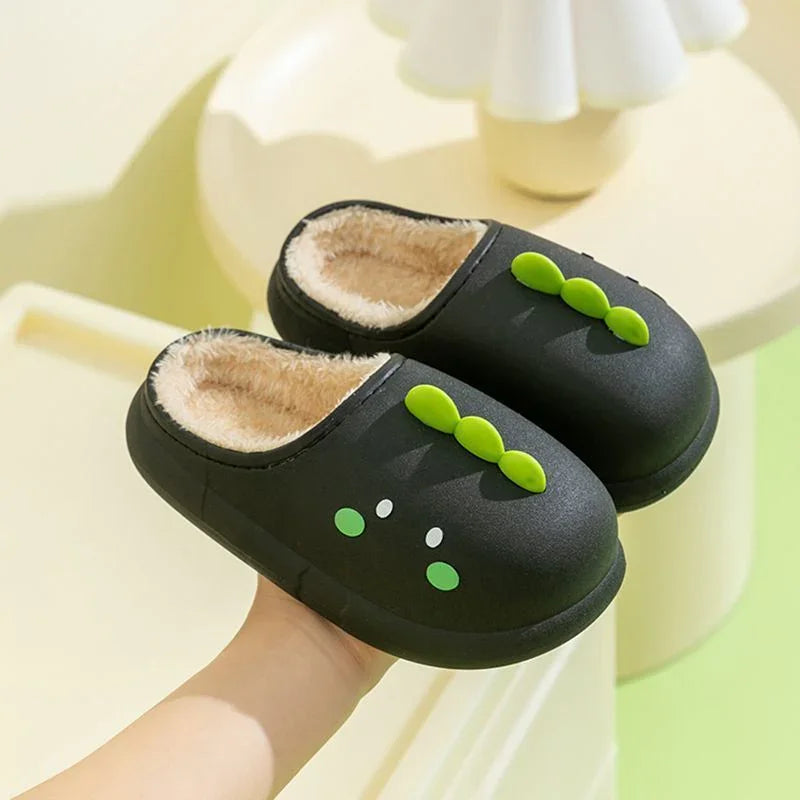 Black indoor slippers with fluffy beige lining and green pea pod design on top, held in hand