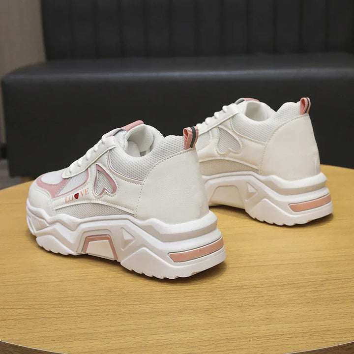 White platform sneakers with pink heart detail and thick sole on wooden table