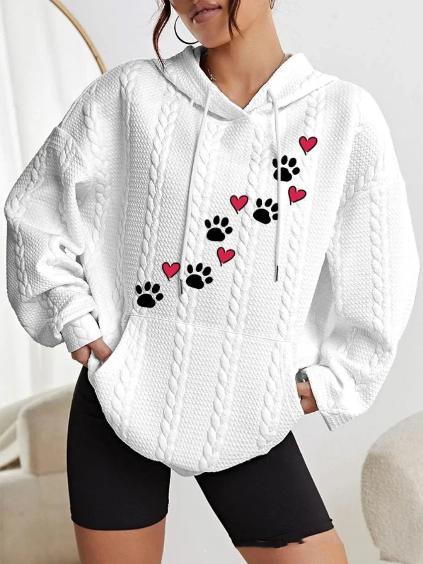 Woman wearing white cable knit hoodie with black paw prints and red hearts design