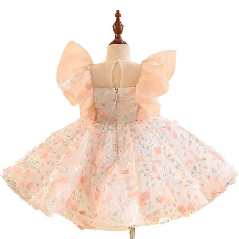 Back view of a toddler's pastel peach floral dress with puff sleeves and glitter details on a mannequin